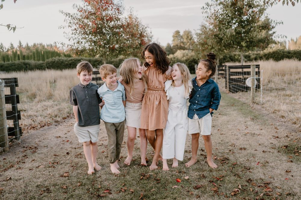 Group shares a candid laughing moment during outdoor photo session in a field.