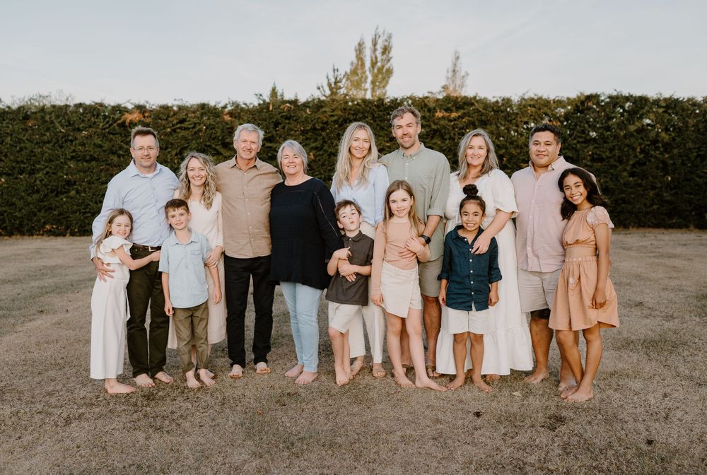 Extended family gathers for a warm sunset portrait against a manicured hedge backdrop.