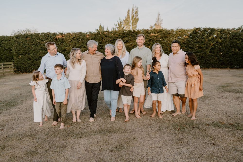 Large family group poses together during golden hour against a tall hedge background.