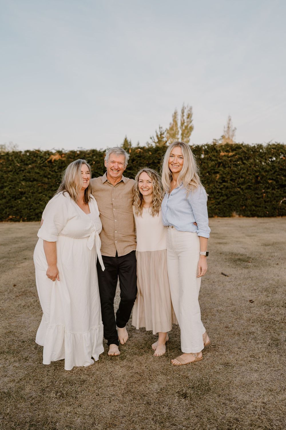 Four people in light neutral clothing pose together outdoors during sunset.