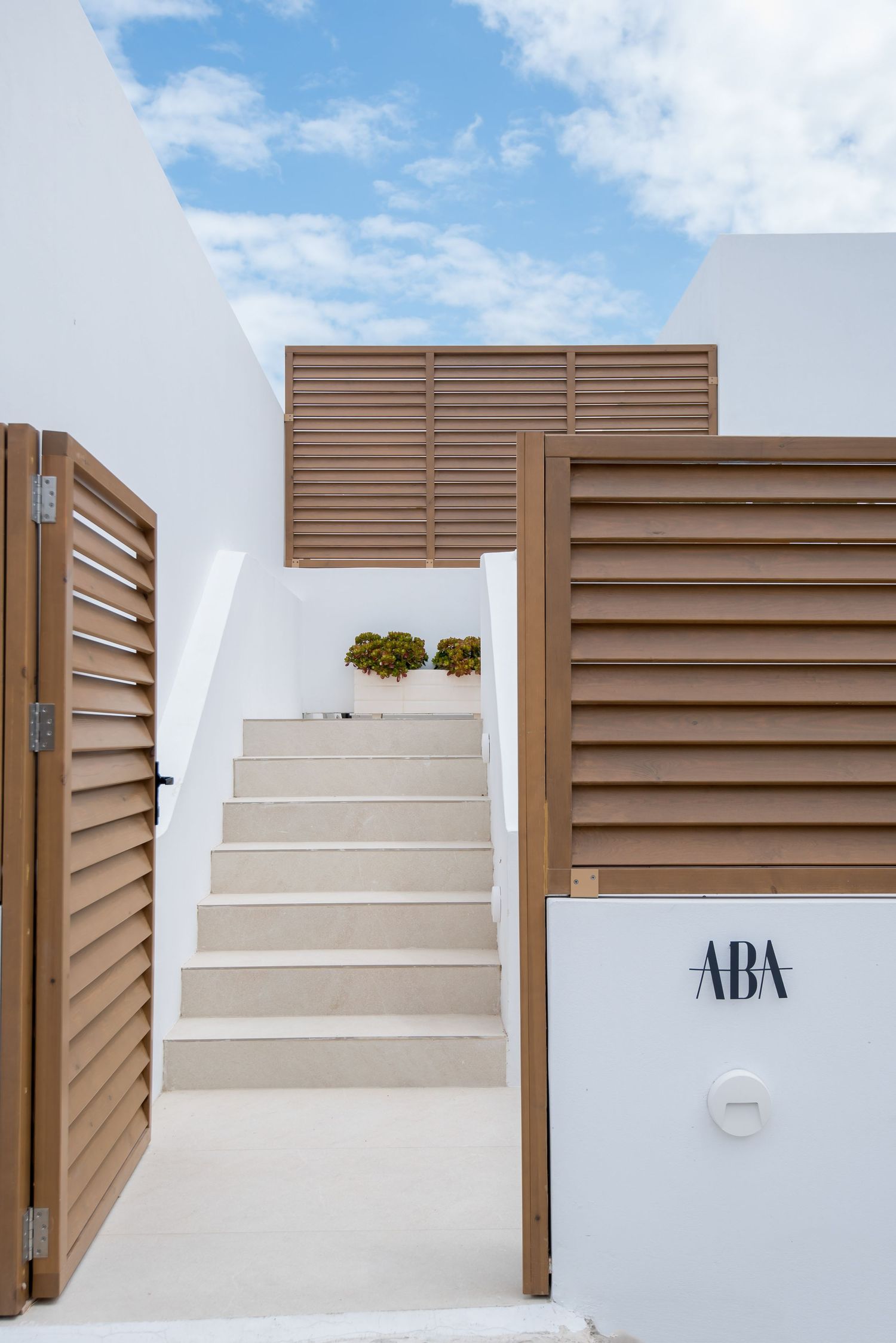 Modern white staircase with brown louvered panels and ABA signage against a bright blue sky.