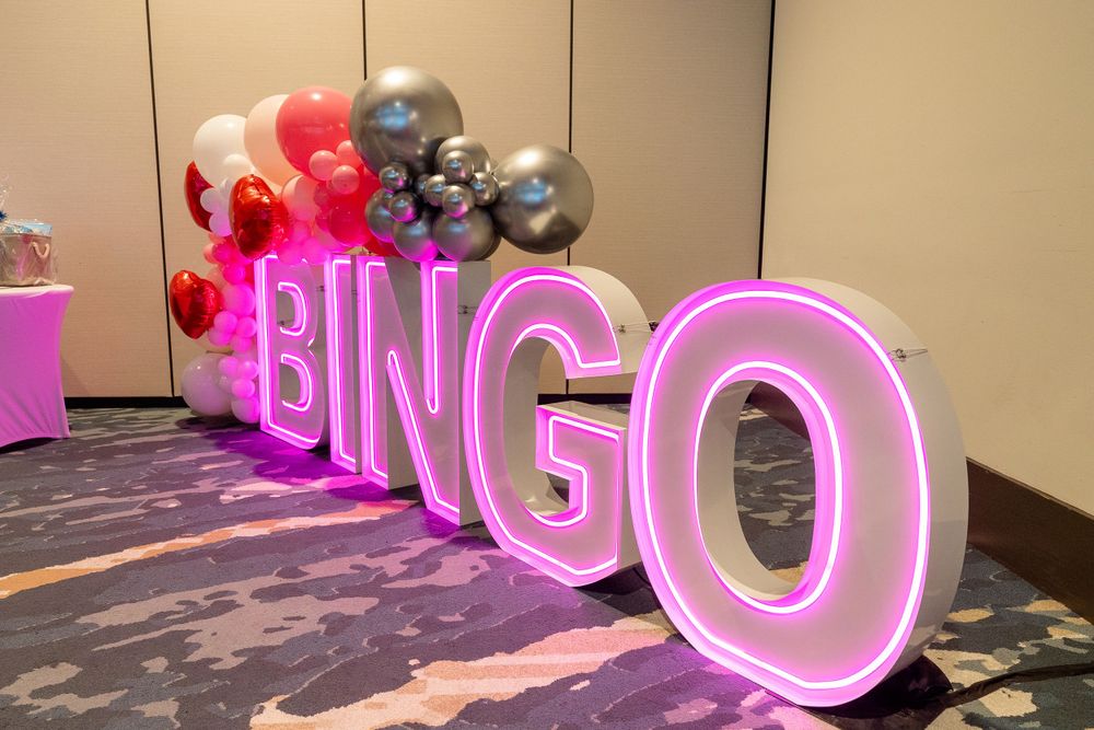 Pink neon BINGO sign with decorative balloons in grey and red colors.