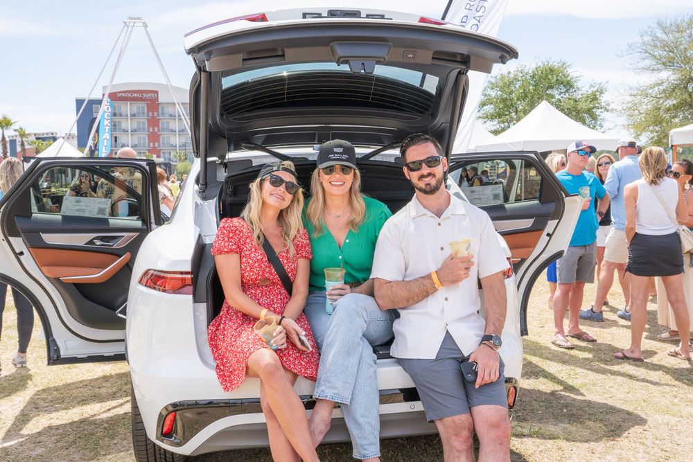 Friends gathered around the back of a white SUV at an outdoor festival event.