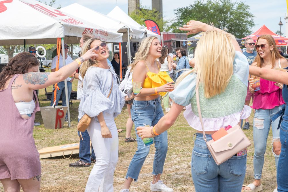 Festival attendees dancing and celebrating outdoors under a bright blue sky.