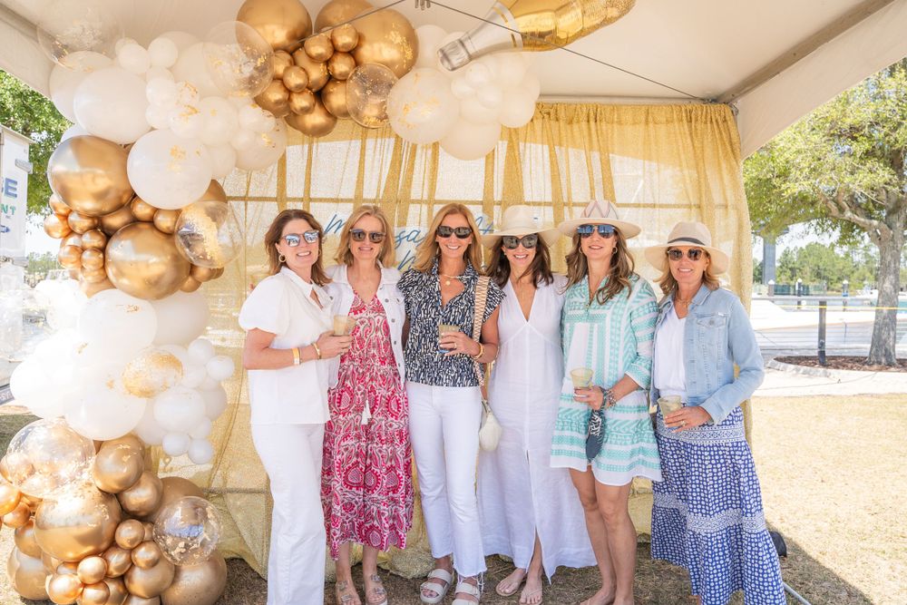 A festive outdoor gathering with gold and white balloon decorations and coordinated summer outfits at a special event.