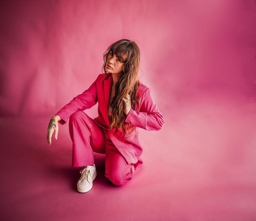 Figure in fuchsia blazer poses dramatically on pink gradient floor.