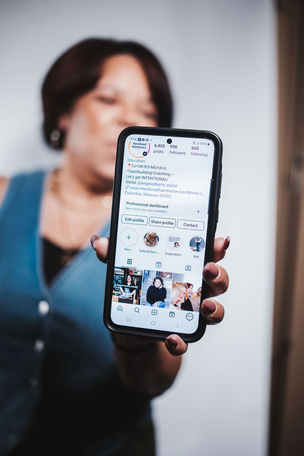 Person holding smartphone displaying social media app interface with grid of photos and messaging features.