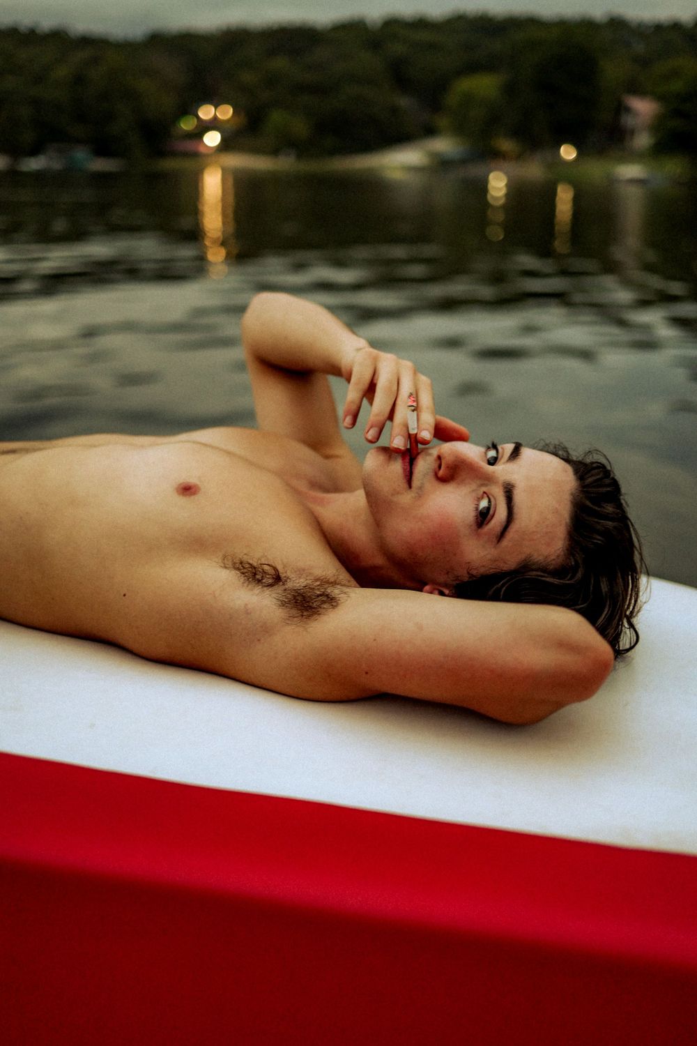 Person reclining on white and red surface near water at dusk.