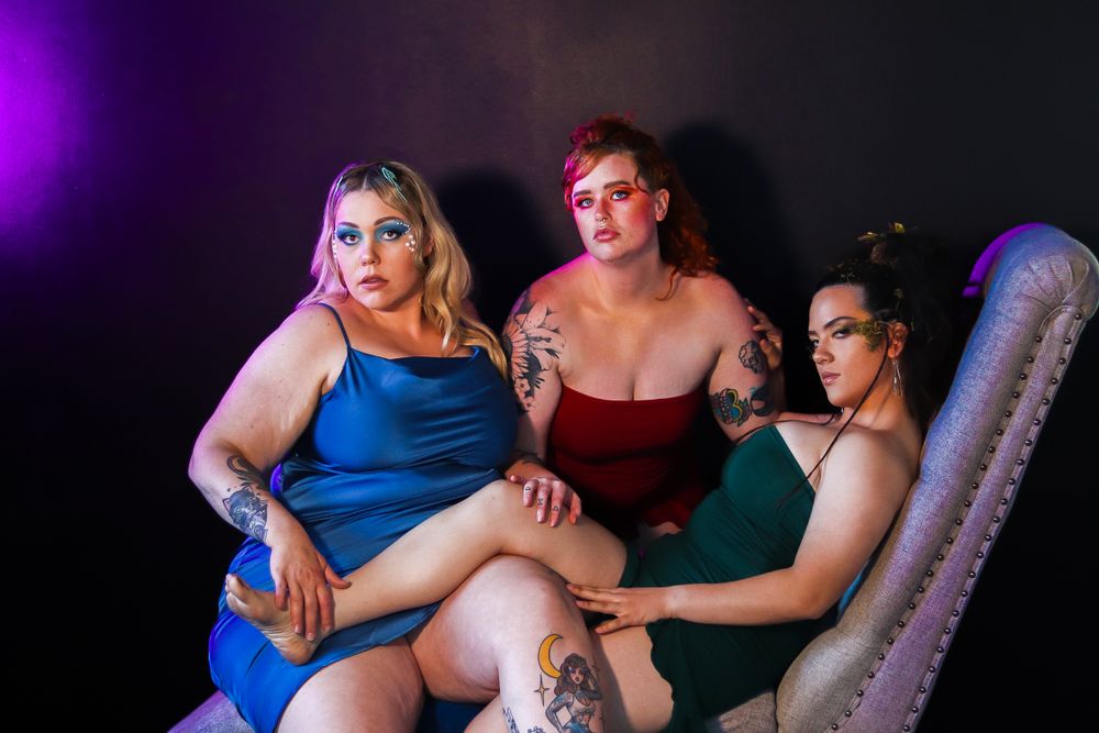 Three people pose on vintage couch with dramatic purple and red lighting effects.