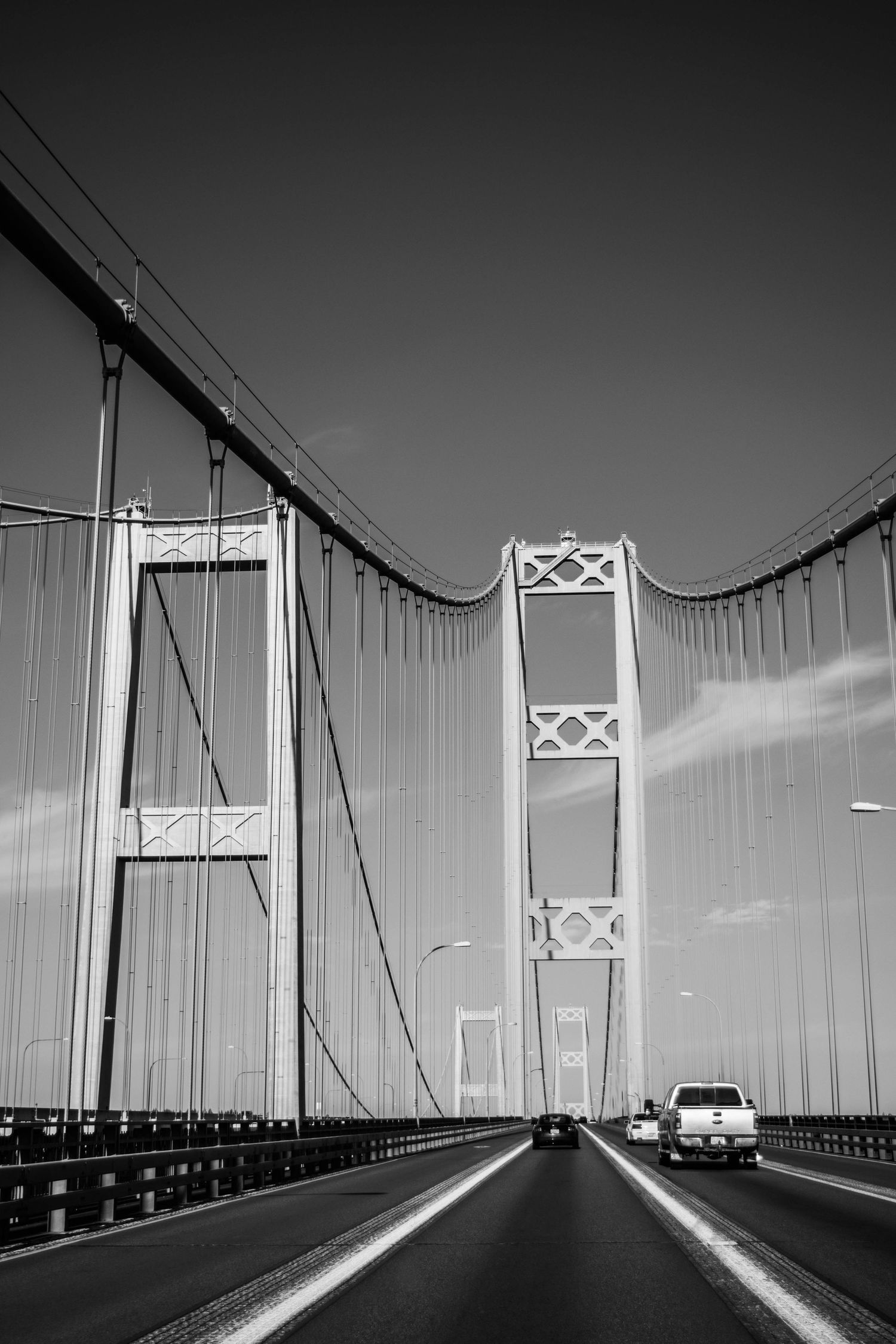Black and white photo of a suspension bridge with a car driving across.