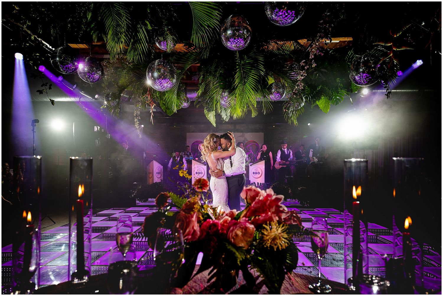 Dramatic purple-lit dance floor with hanging disco balls and tropical greenery overhead.