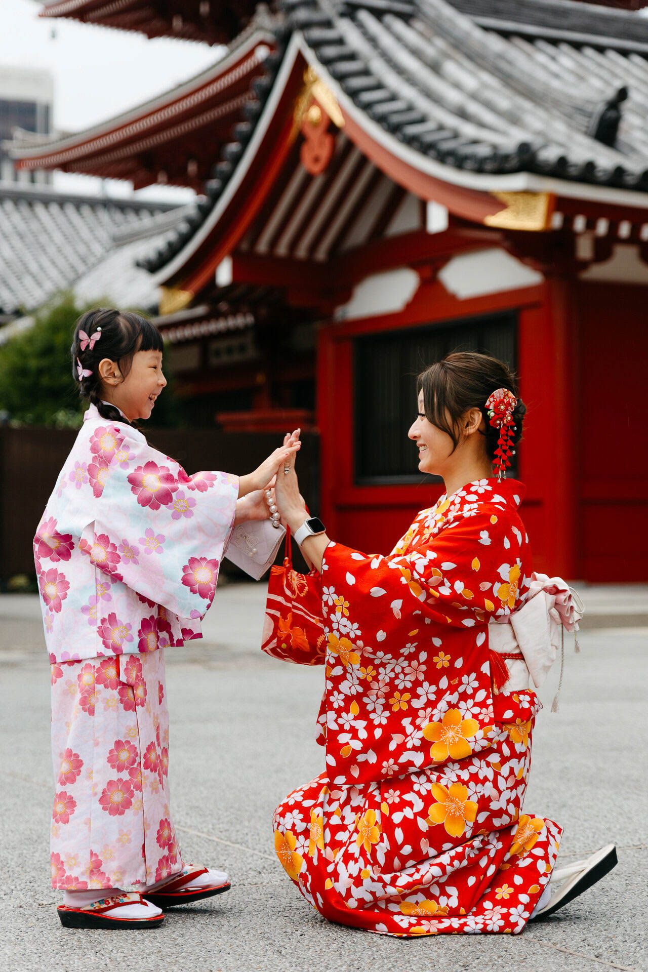 Two people in colorful kimonos play a hand game outside a traditional Japanese temple.
