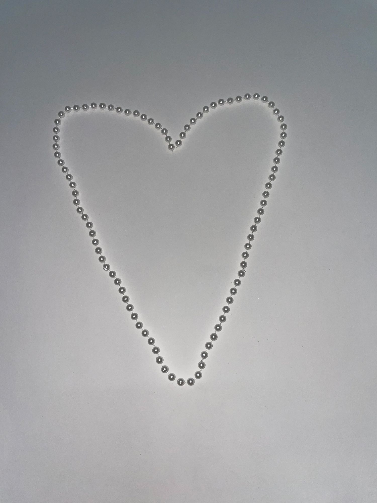 Heart shape made from silver metallic beads against a gray background.