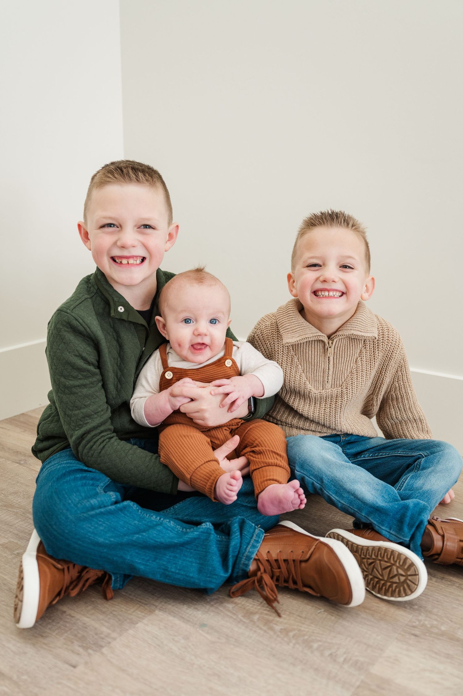 Sibling portrait of three children sitting on floor in casual sweaters.