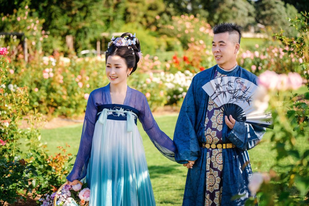 Dynamic natural sunlight portrait of a couple hugging and dancing in Tang Dynasty Hanfu among blooming roses, by Imagine Image Studio.