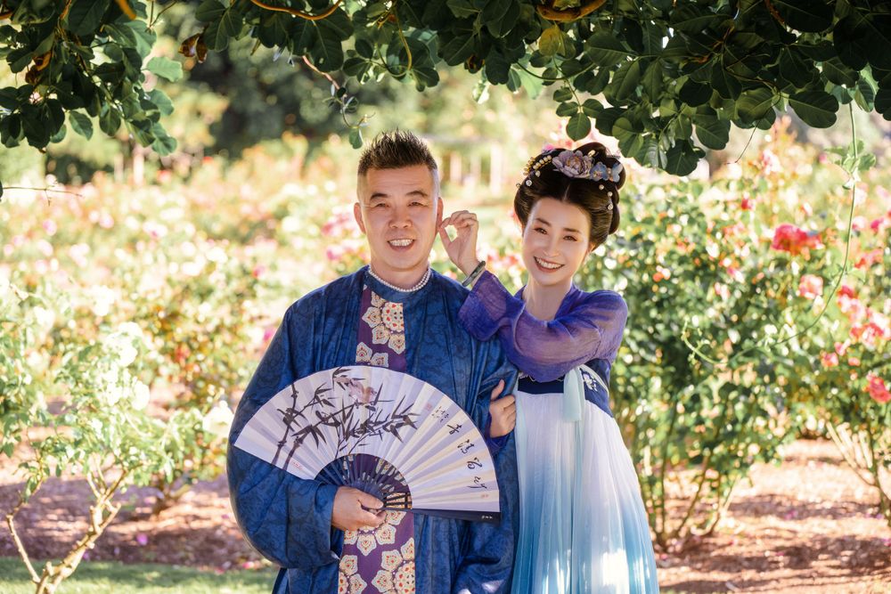 Dynamic natural sunlight portrait of a couple hugging and dancing in Tang Dynasty Hanfu among blooming roses, by Imagine Image Studio.