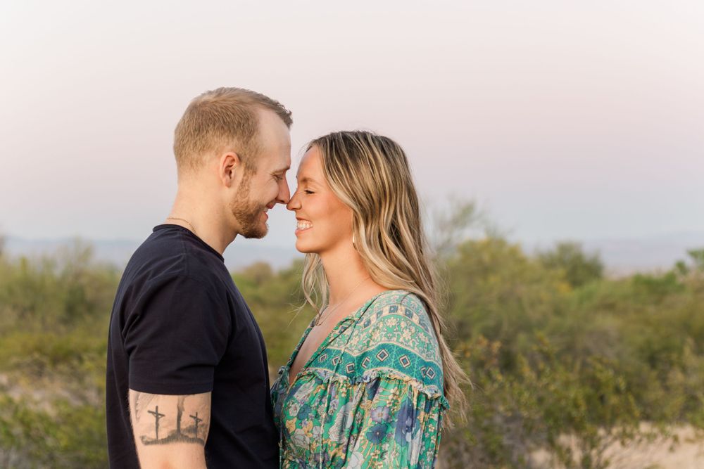 Couple embracing in desert setting wearing green floral dress and black shirt.