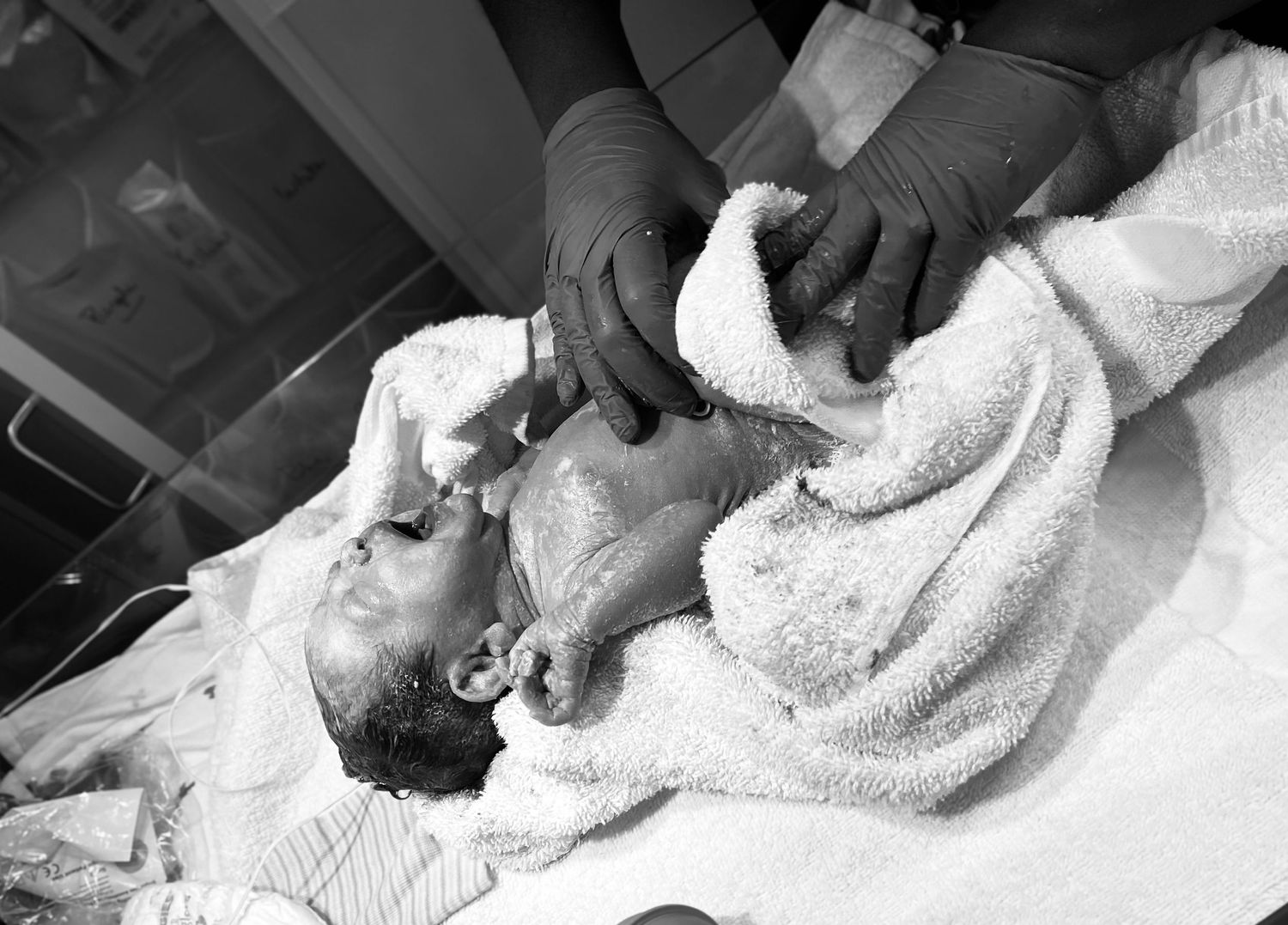 Medical professional attending to a newborn baby wrapped in a white towel.