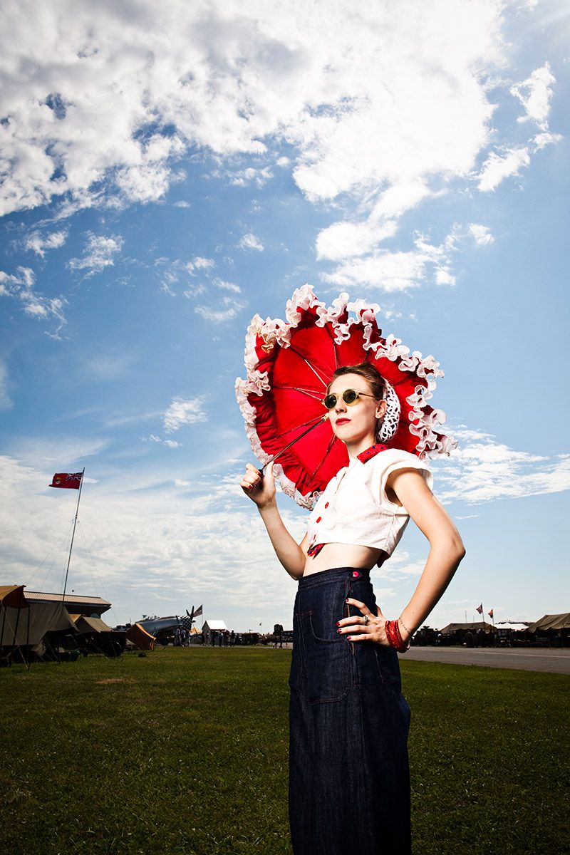 Woman in vintage style holding red parasol umbrella outdoors under blue sky.