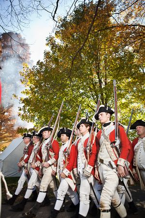 British Redcoat soldiers marching in Revolutionary War reenactment with muskets raised.