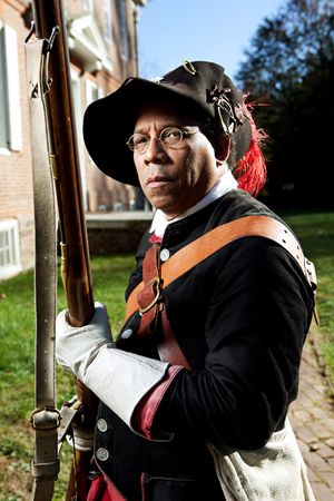 African American man in colonial militia uniform holds a musket during a Revolutionary War reenactment.