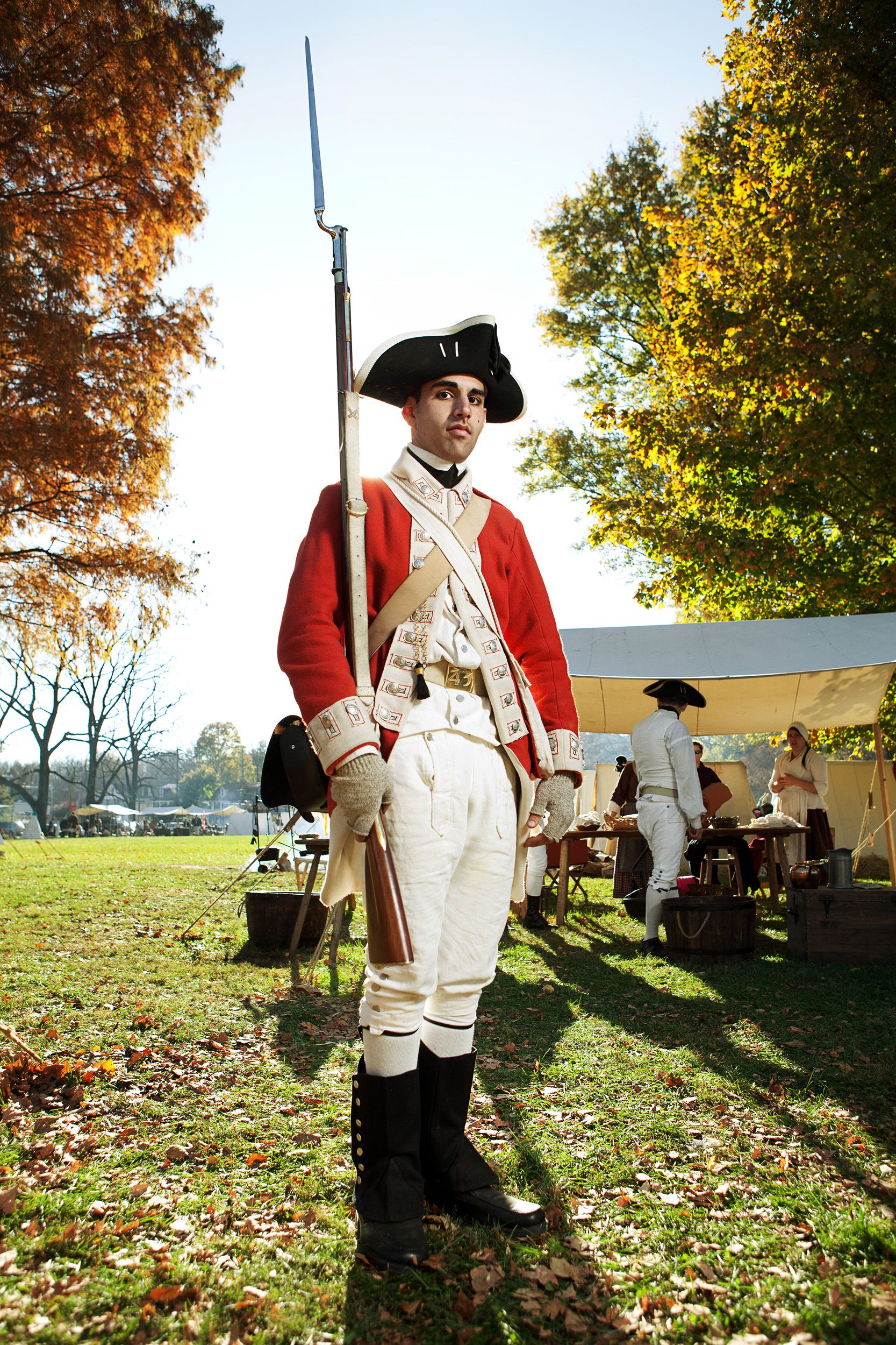 Man in British redcoat uniform holding musket at Revolutionary War reenactment outdoors.
