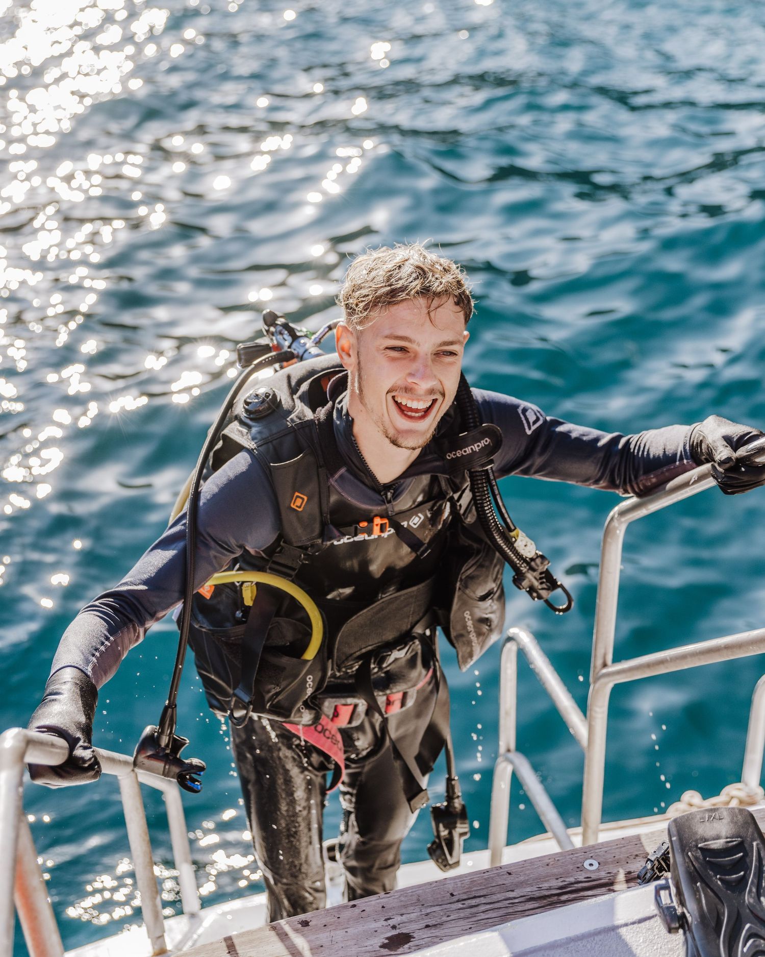 happy male scuba diver exiting water walking up ladder of sailing dive charter boat Airlie Beach the whitsunday islands