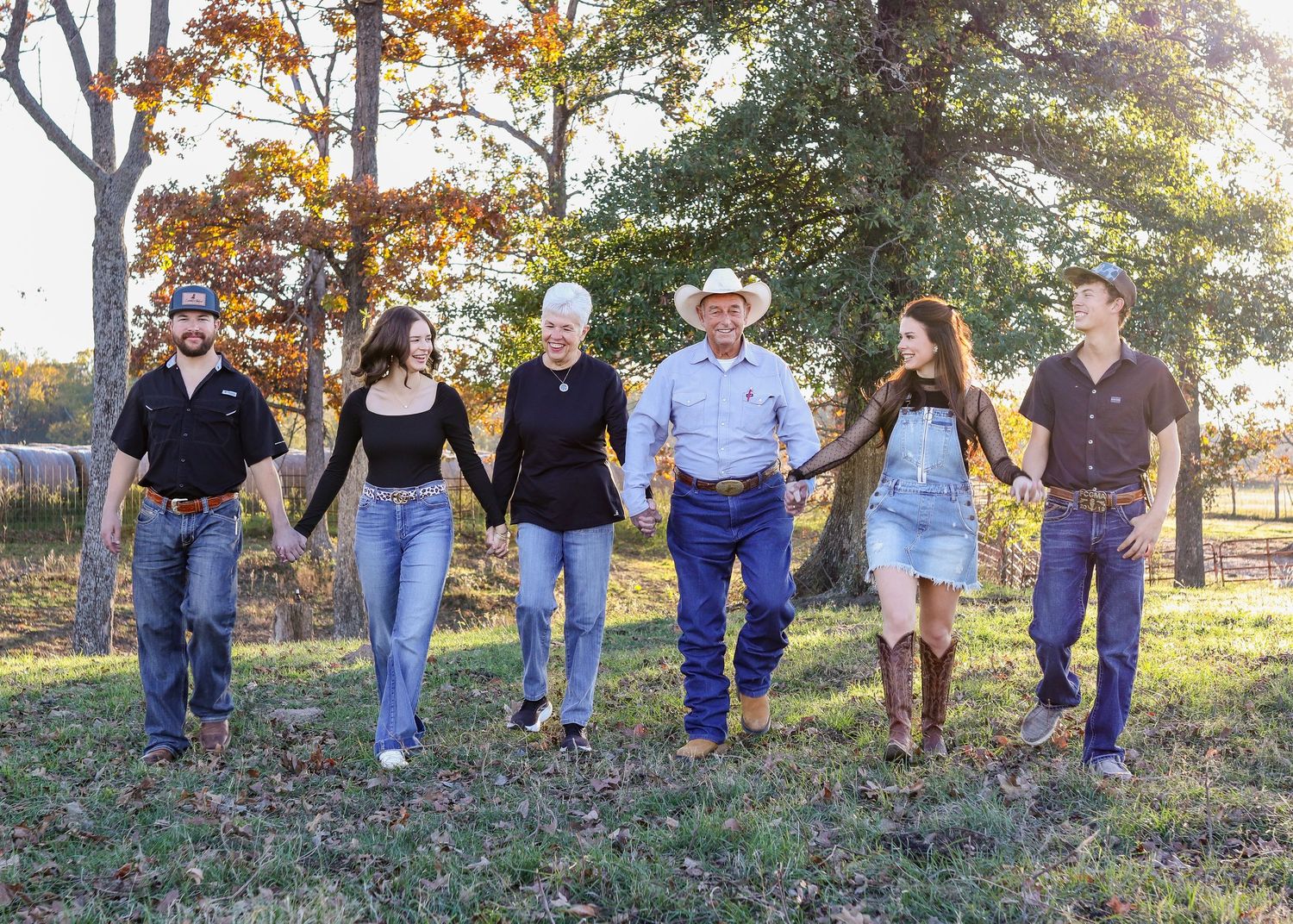 Six family members holding hands and walking together through a colorful autumn outdoor setting.