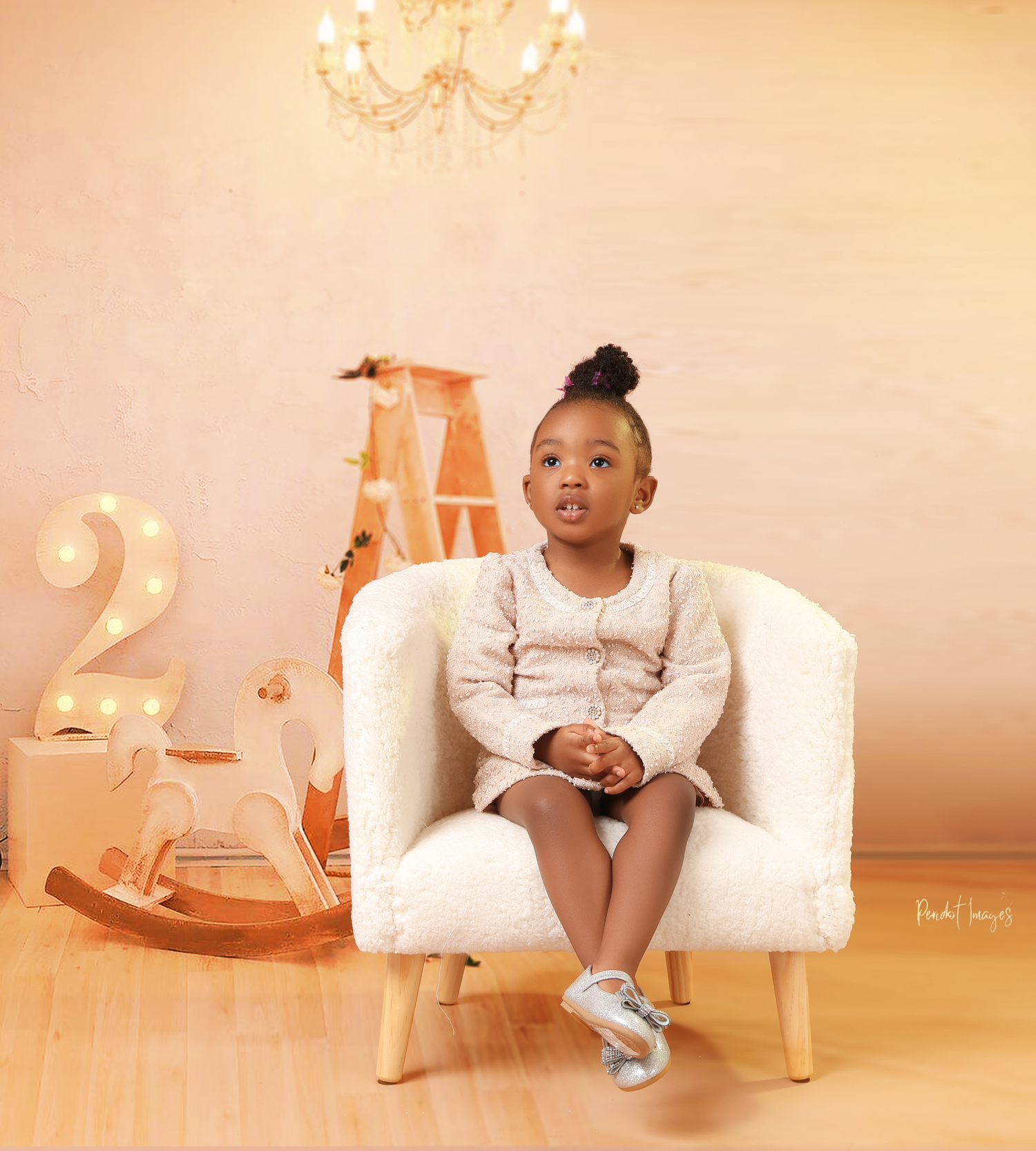 Child sits in white armchair with rocking horse and number 2 decoration in background.