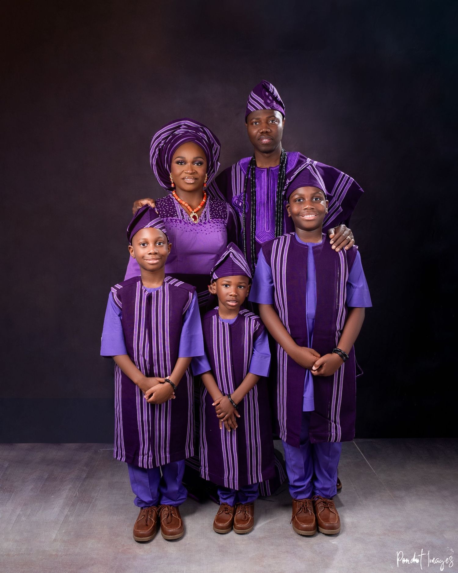 A group wearing matching purple and black traditional African attire poses together in a studio setting.