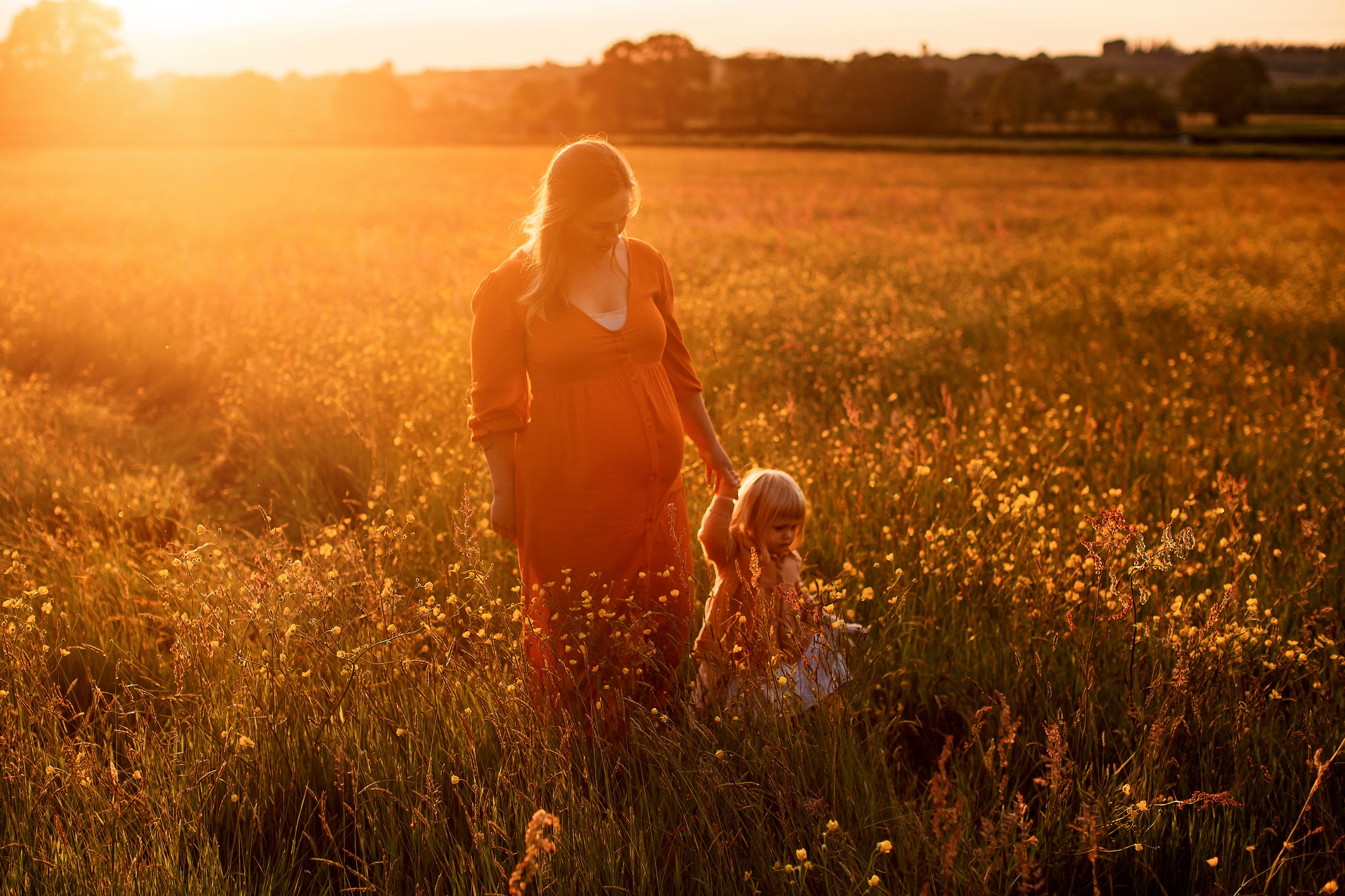 Golden hour maternity photography of pregnany mother and her young daughter in wildflowers