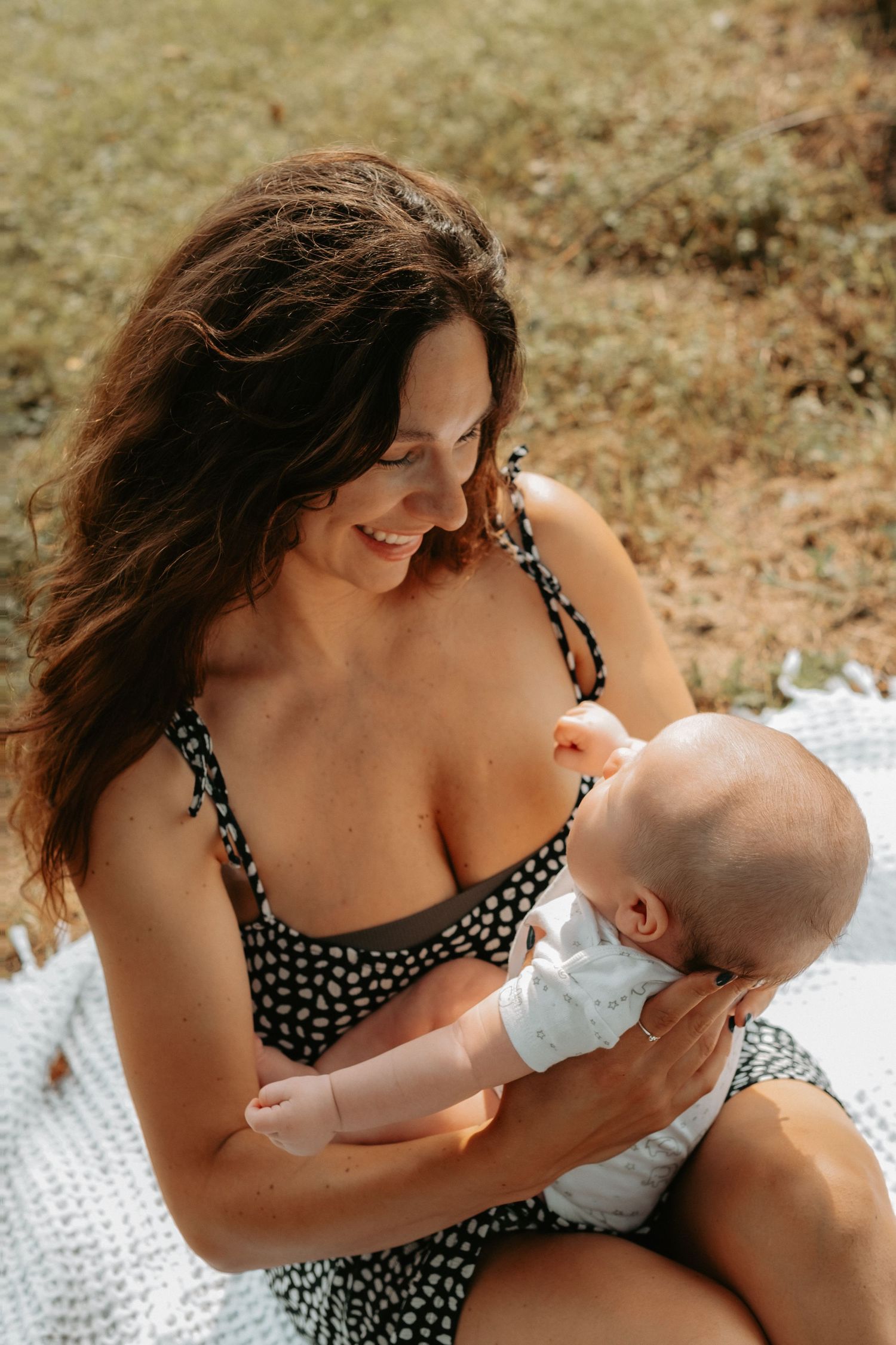 A tender moment shared between a parent in a polka dot dress and their infant baby on a white blanket outdoors.