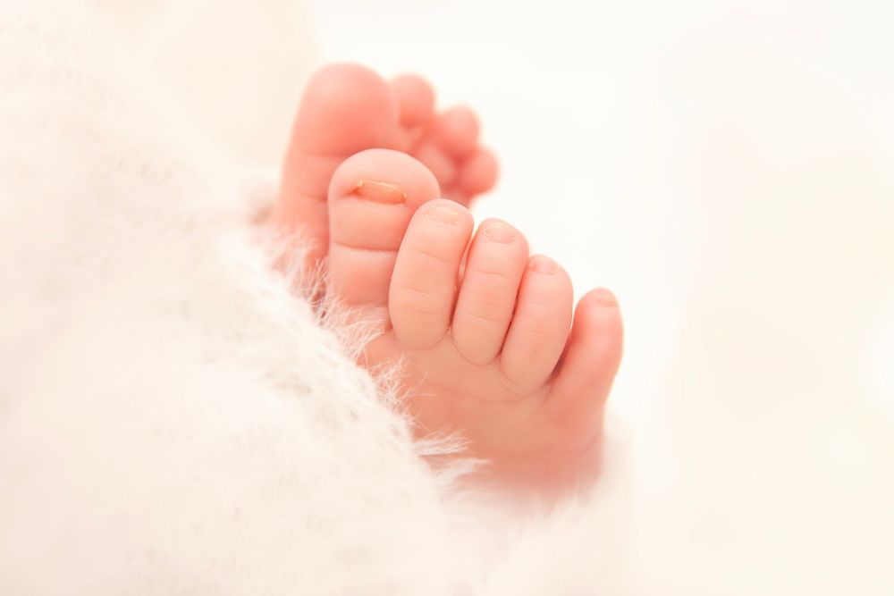 Close-up of tiny newborn baby toes resting on soft white fluffy blanket.