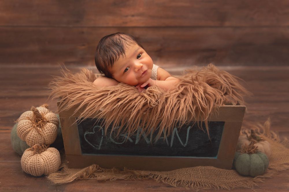 Smiling newborn baby resting in wooden crate with name Jonan on chalkboard.