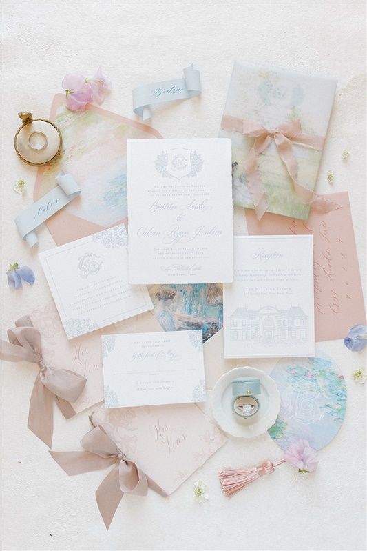 Elegant wedding stationery flatlay with white invitations, pastel ribbons, and delicate floral details on a light background.