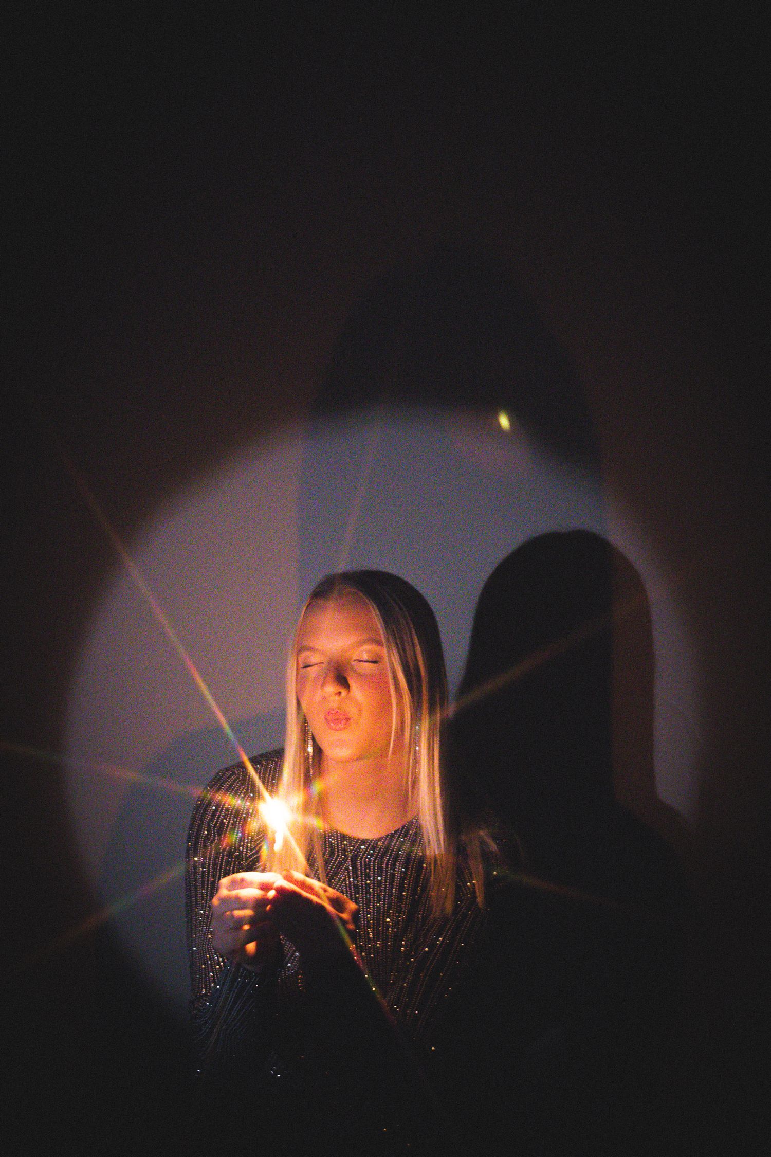 Artistic portrait of person holding sparkler in dark with light flares.