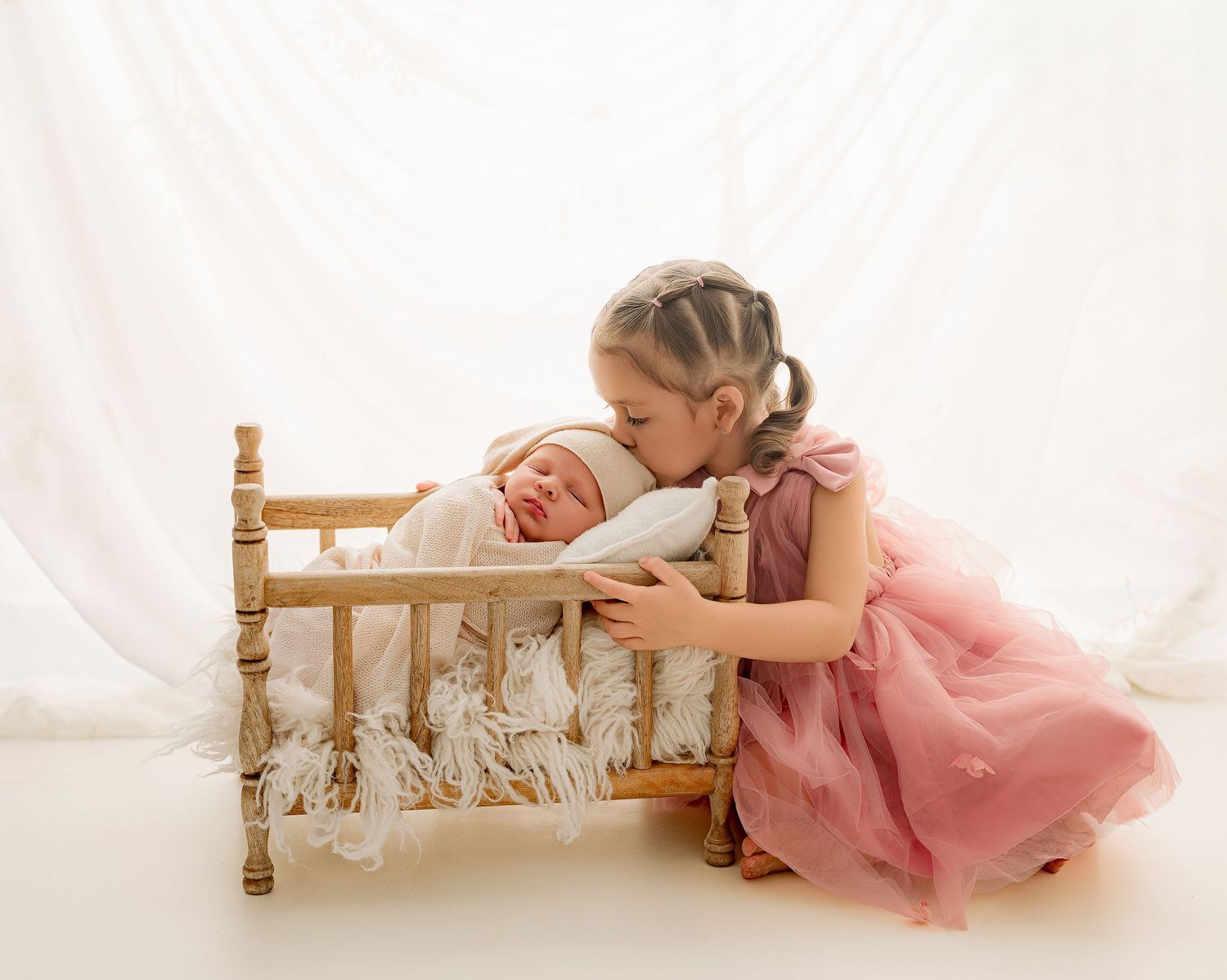 A series of photos showing a baby in a pink dress lying on a white blanket near a wooden bench.