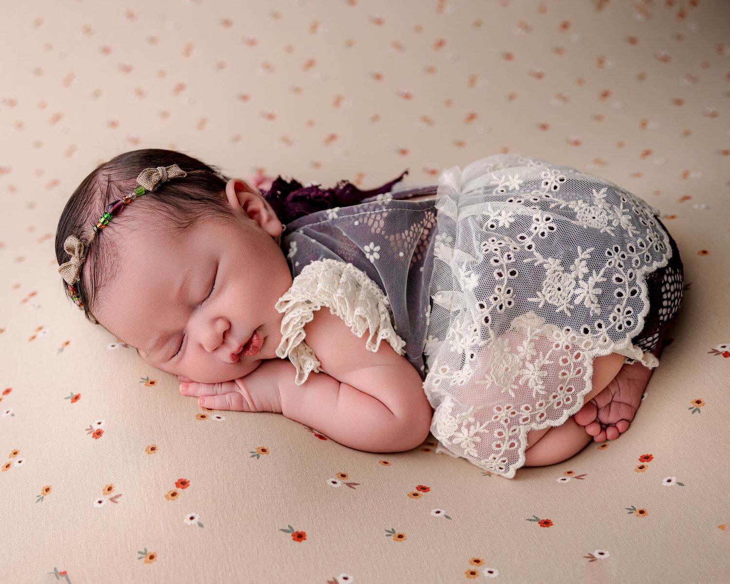 Sleeping newborn in lace outfit on polka dot background with delicate styling.