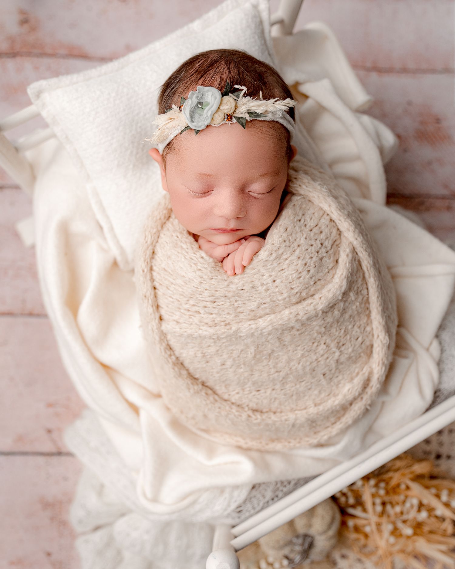 Newborn baby wrapped in cream colored knit blanket sleeping peacefully on white textured backdrop.