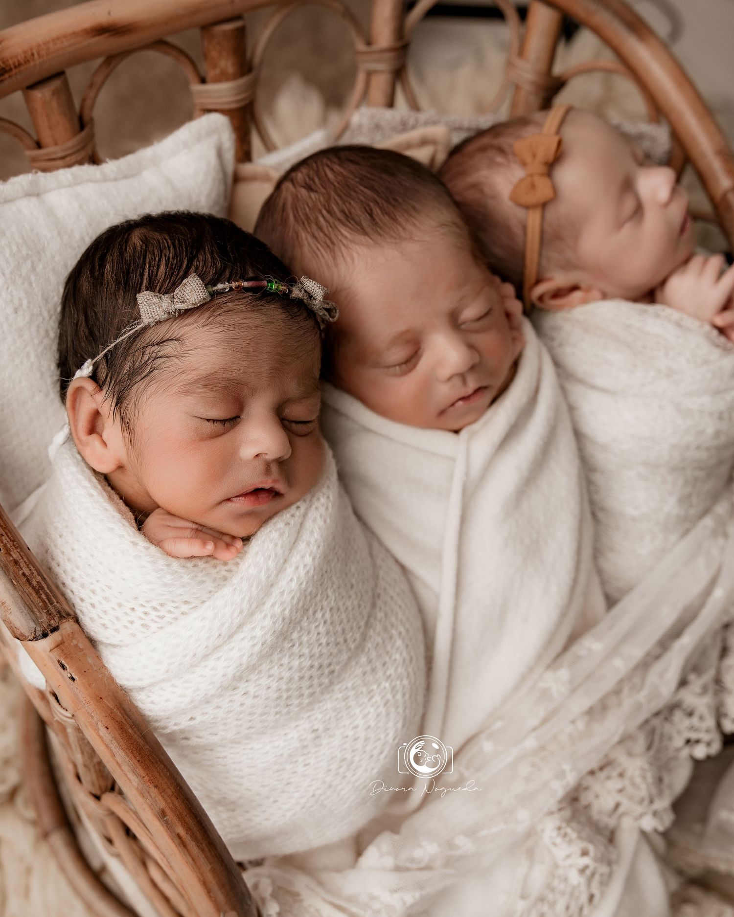 Three sleeping newborn babies wrapped in white blankets rest together in a woven basket.