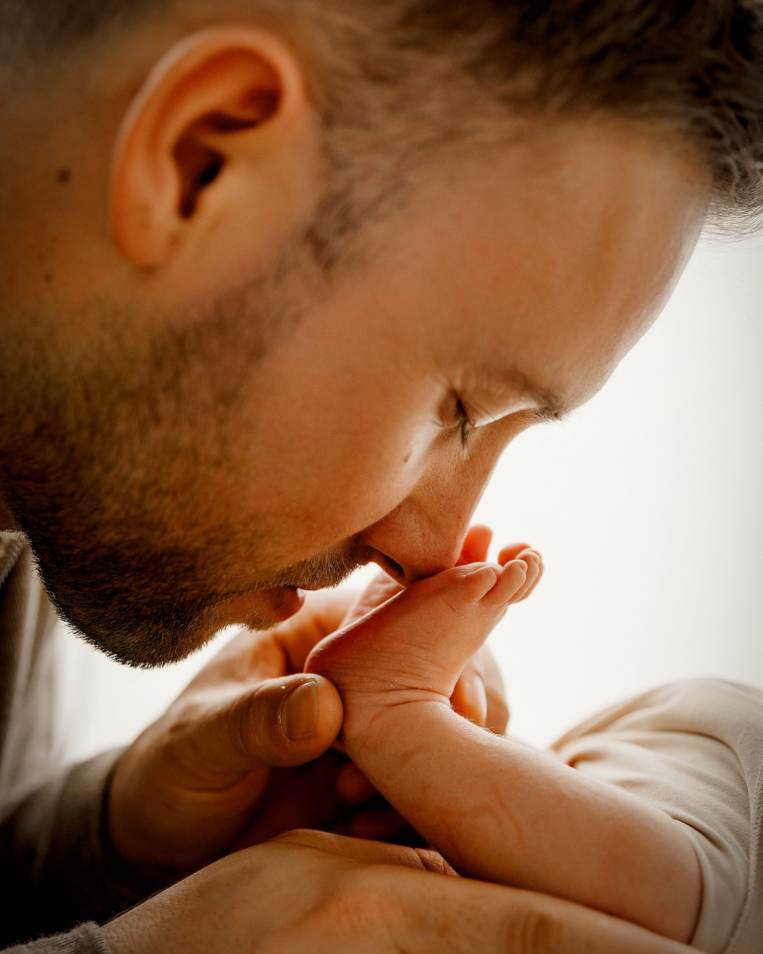 A bearded father tenderly kisses his newborn baby's tiny hand in a warm, intimate close-up portrait.