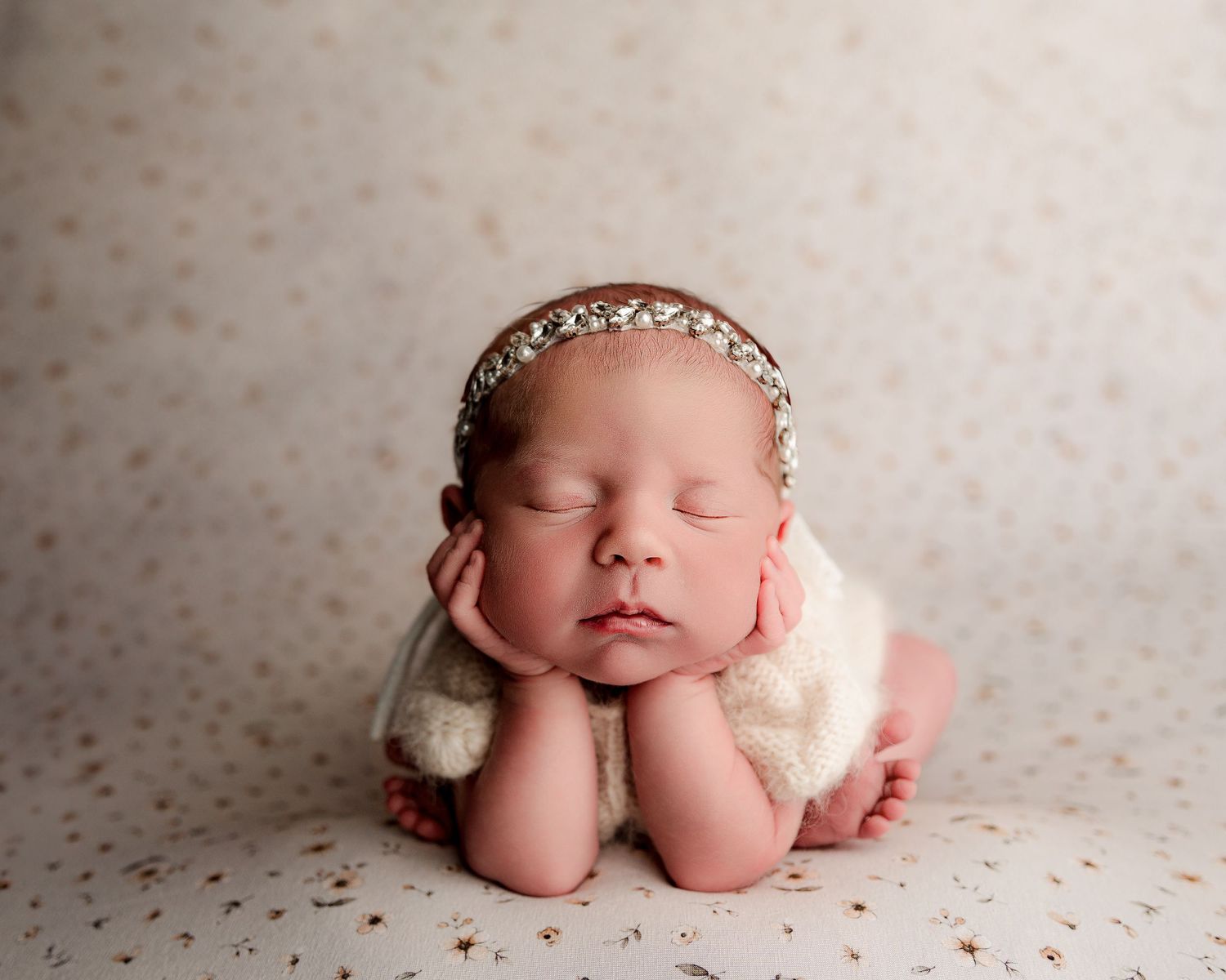 Peaceful newborn portrait with delicate headpiece resting on spotted background.
