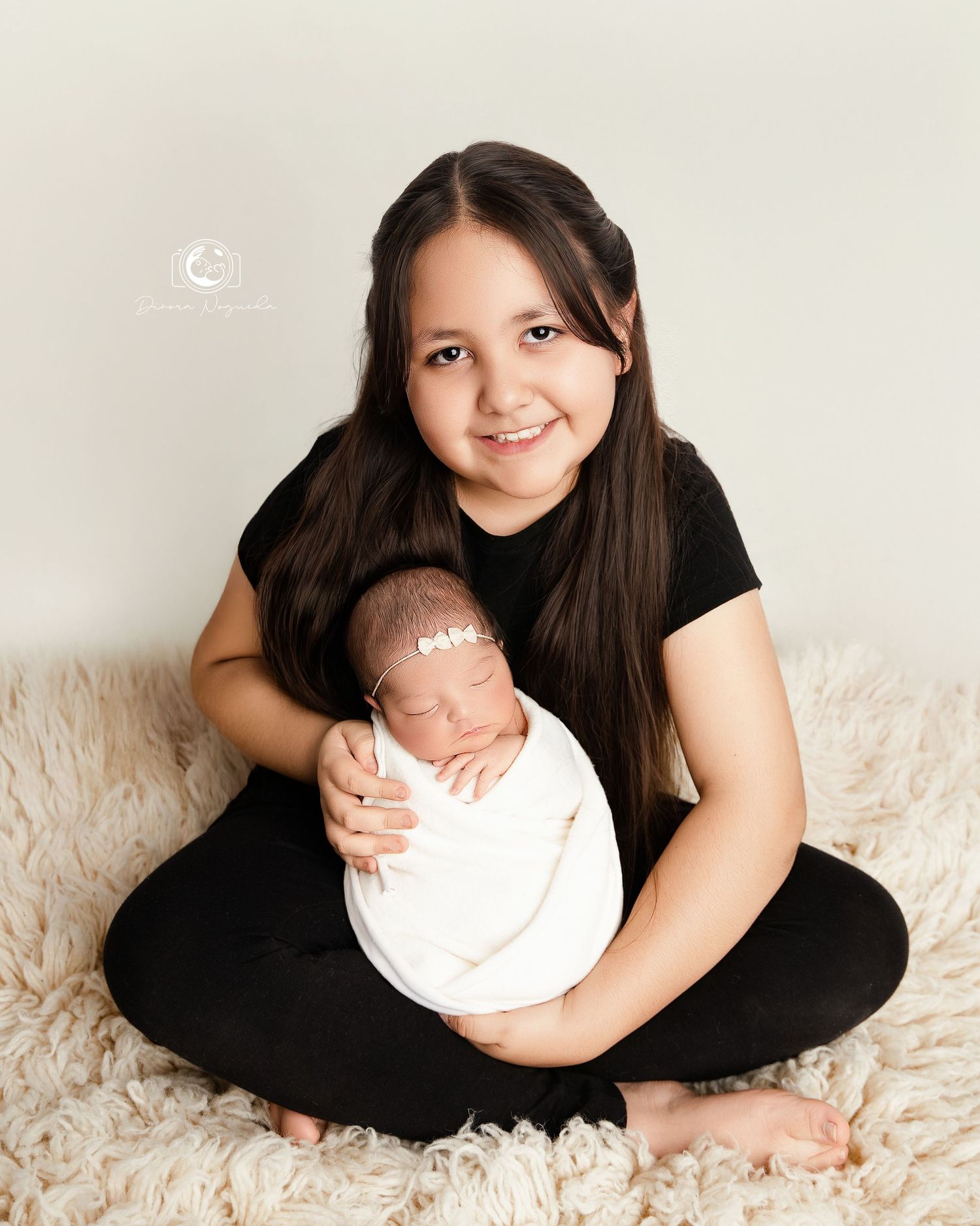 Mother in black dress sitting on white carpet holding newborn baby in artistic poses for photography session.