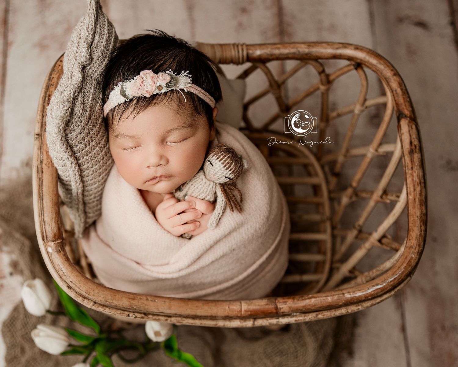 Sleeping newborn swaddled in soft fabric rests peacefully in vintage wicker basket during professional photography session.