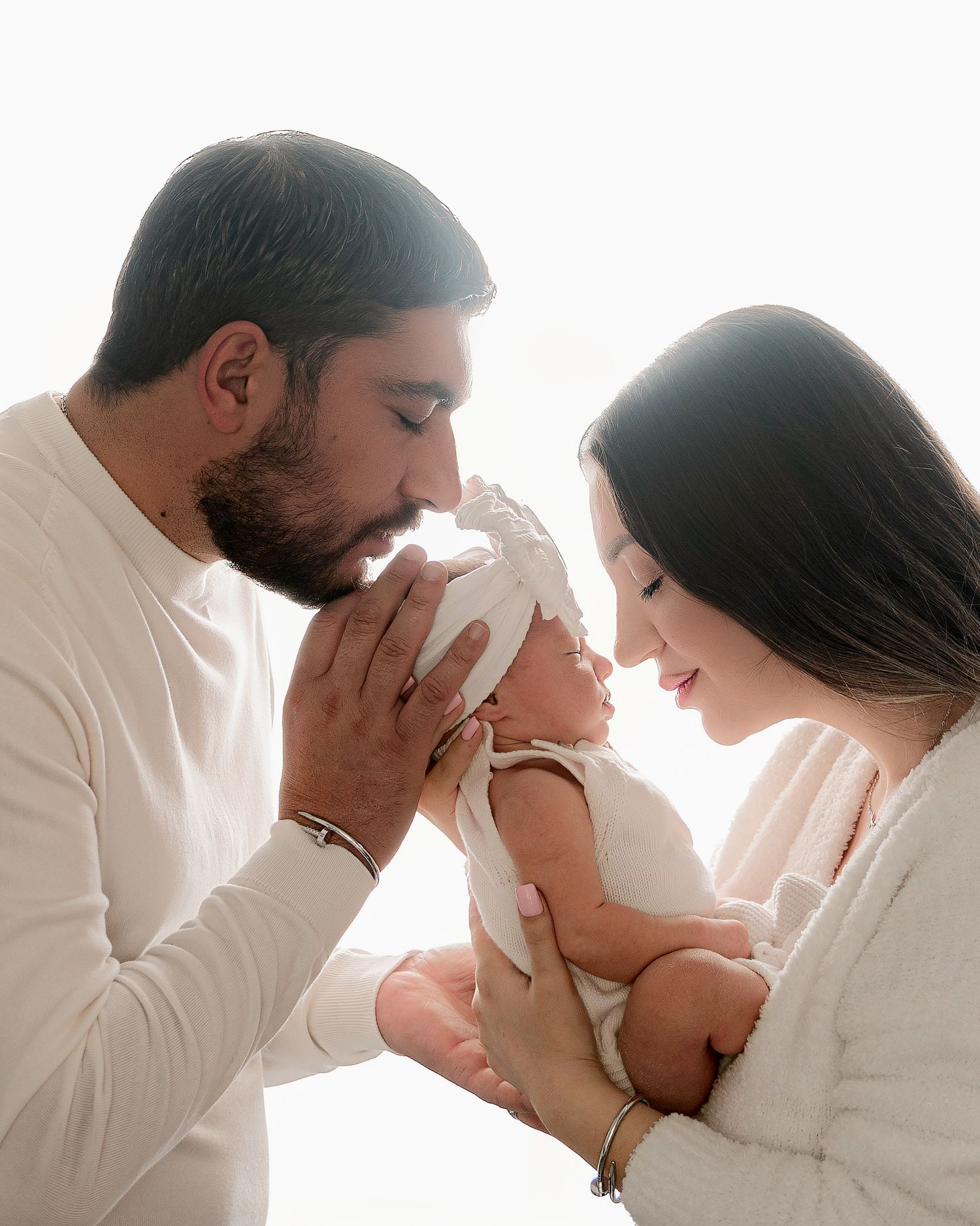 Parents sharing intimate moment with newborn baby against white background.