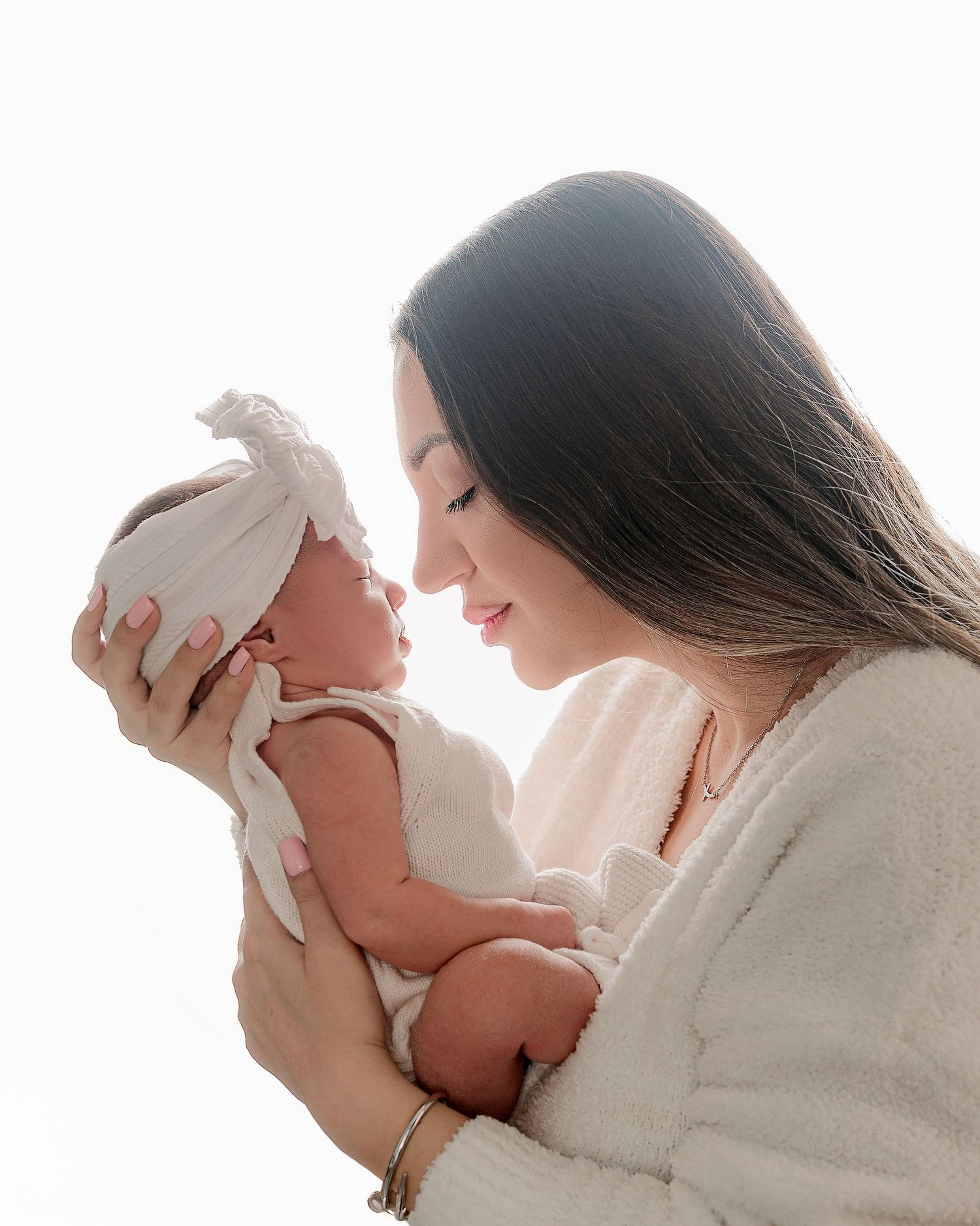 Mother in white sweater holding newborn baby in intimate portrait.