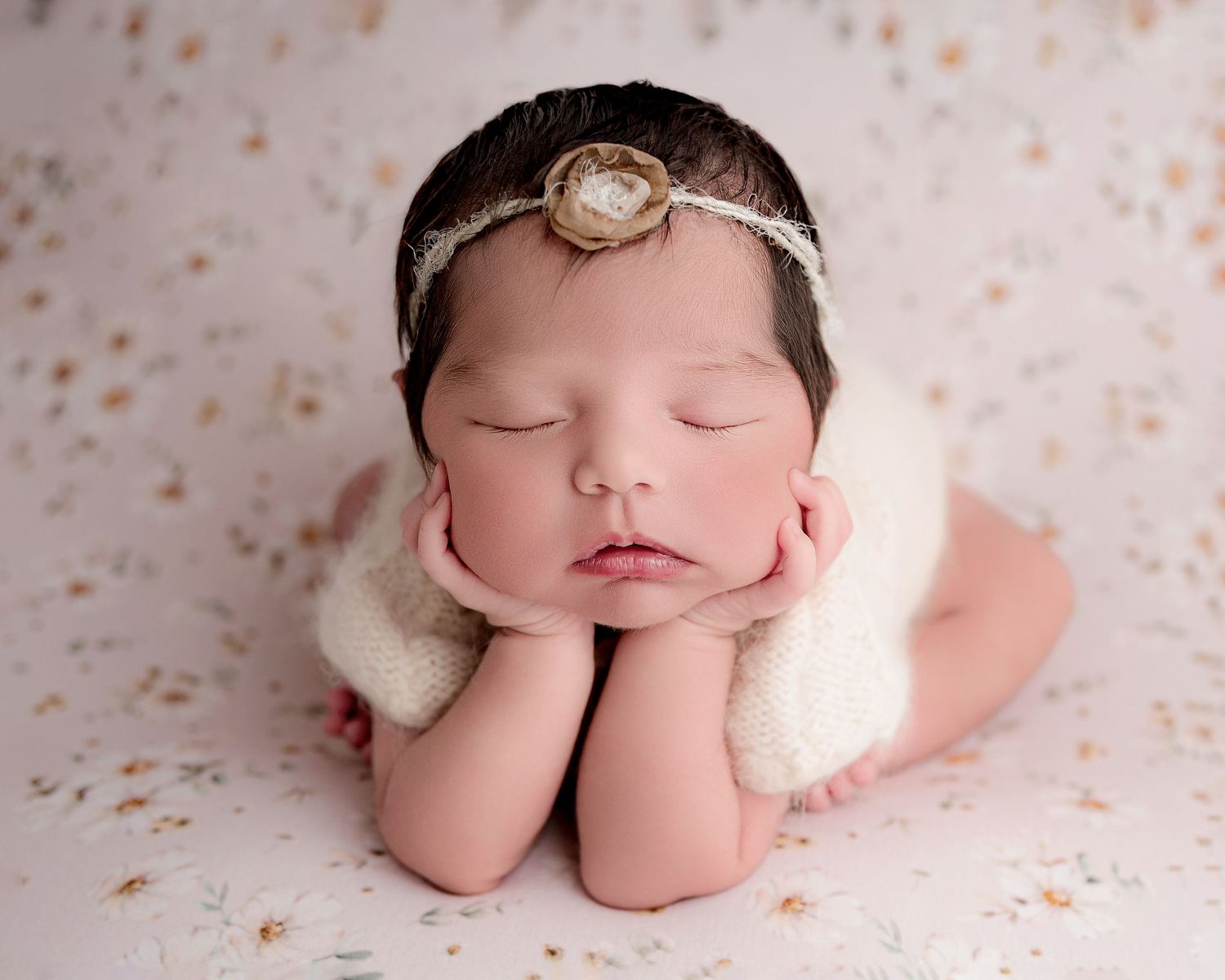 A sleeping newborn wearing a delicate white headband rests peacefully on a polka dot backdrop.
