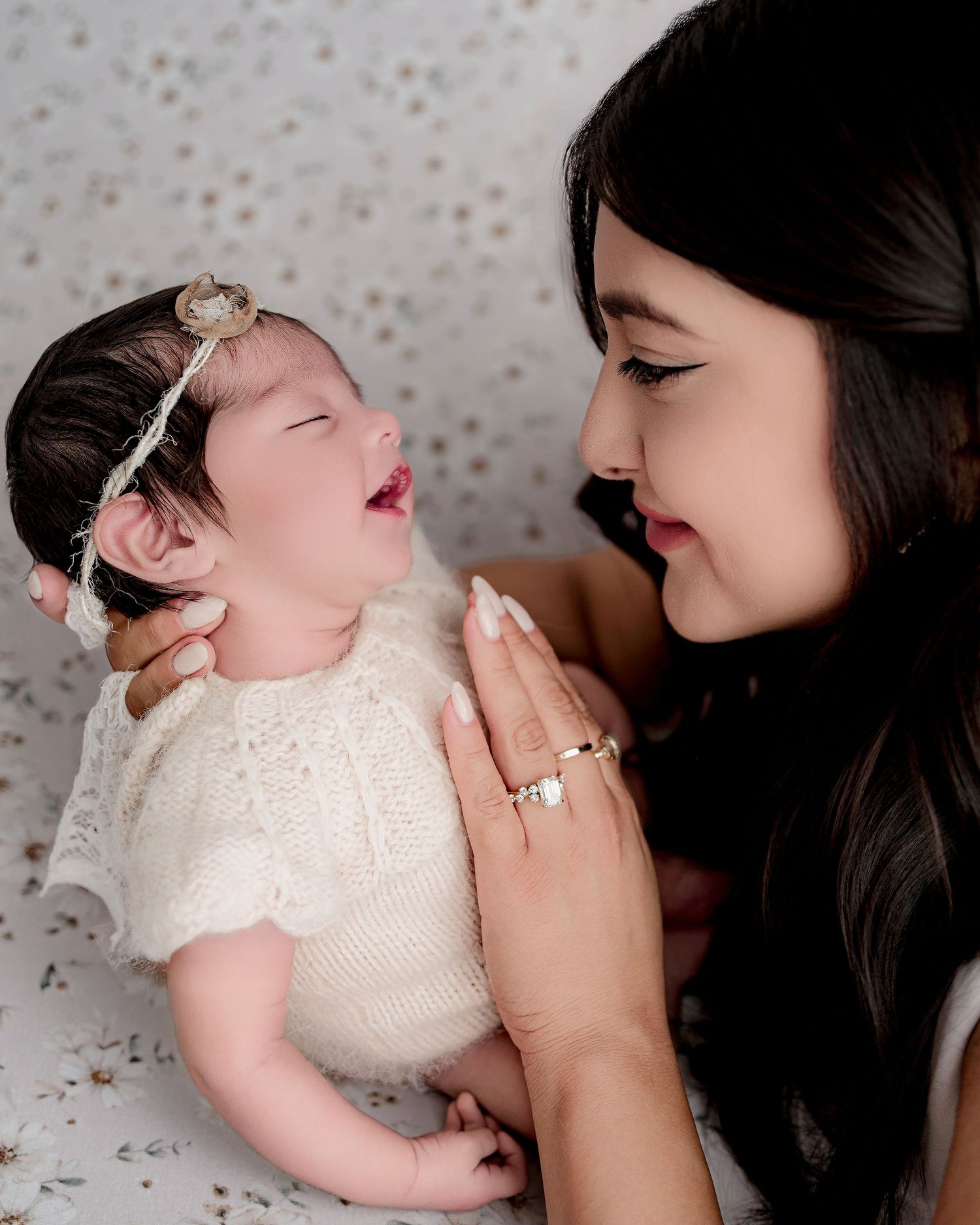 A tender moment shared between a mother and baby in white against a light gray background.