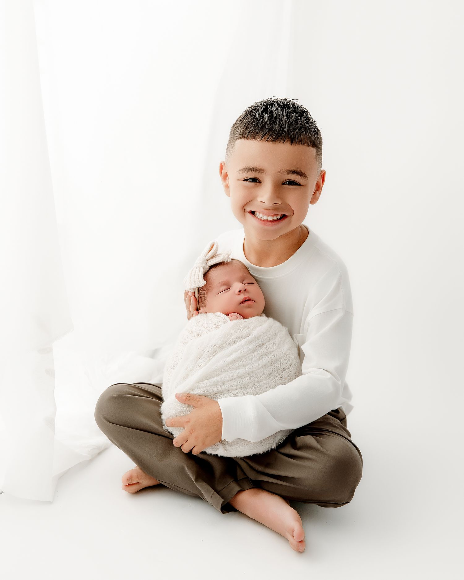 Two siblings share a tender moment together on a white background.