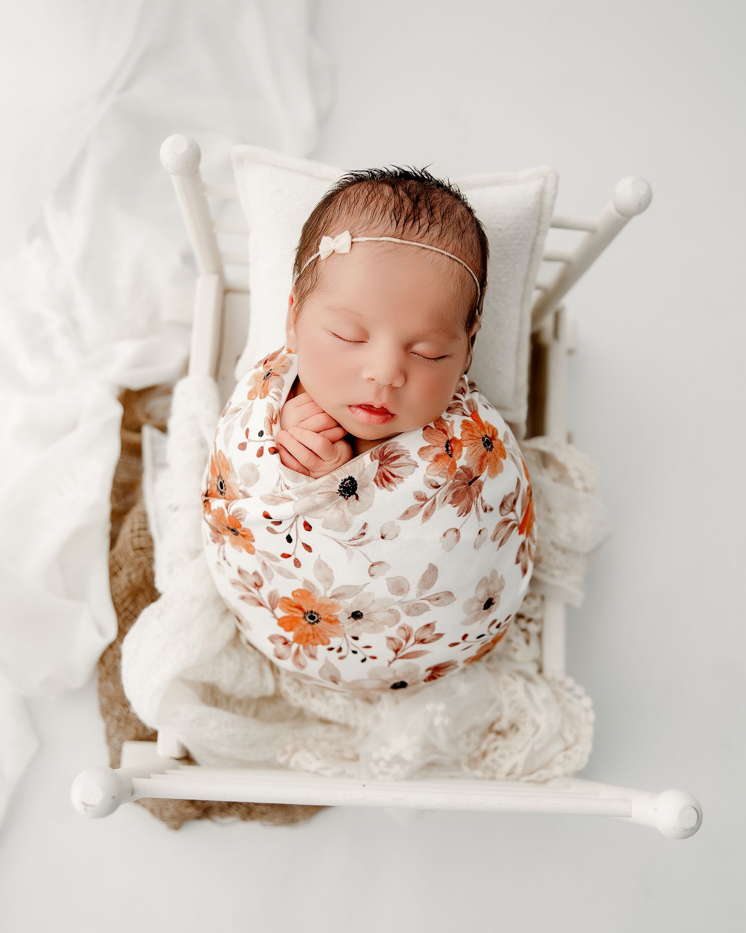 A sleeping newborn baby wrapped in a floral print blanket lies peacefully on white bedding.